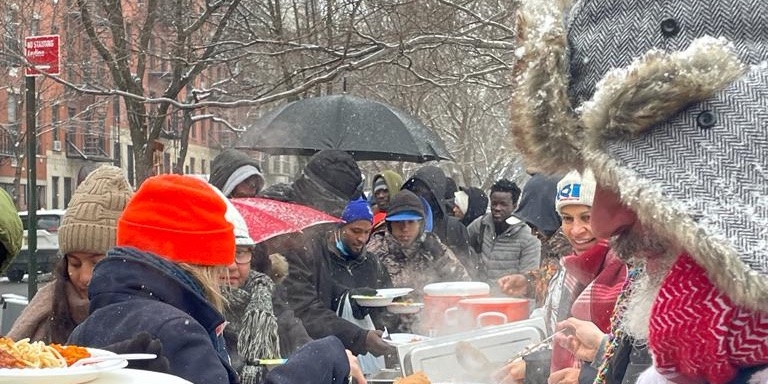 A group of volunteers serves hot food to migrants waiting for shelter bed assignments, Tompkins Square Park, winter 2024